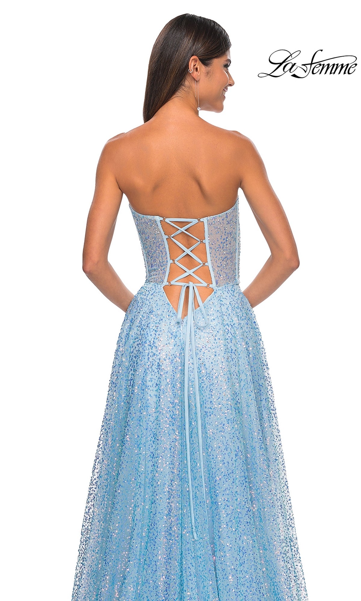 A woman poses with her back to the camera in the La Femme Strapless Embellished Prom Dress 32136, a long A-line gown with glittery light blue fabric, hot-stone details, and a lace-up back.